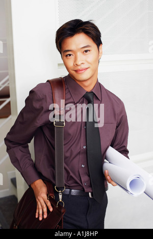 Portrait of a male architect holding rolled up blueprints and smiling Stock Photo