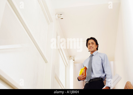Low angle view of a male architect holding rolled up blueprints and a hardhat Stock Photo
