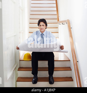 Portrait of a male architect holding blueprints on a staircase Stock Photo
