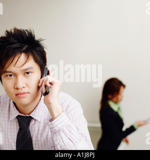 Portrait of a businessman talking on a mobile phone with a businesswoman in the background Stock Photo