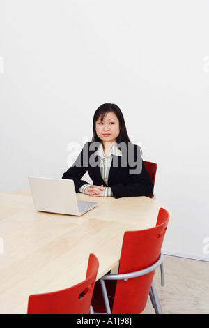 Businesswoman sitting with a laptop in a board room and looking away Stock Photo