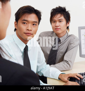 Two businessmen and a businesswoman sitting together in an office Stock Photo