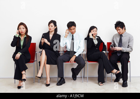 Two businessmen and three businesswomen sitting with mobile phones Stock Photo