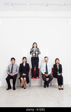 Portrait of a businesswoman standing on an armchair with four business executives sitting beside her Stock Photo