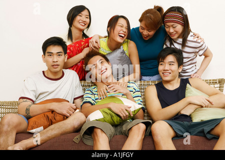 Close-up of three young men sitting on a couch with four women standing behind them Stock Photo