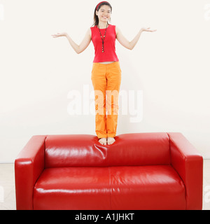 Portrait of a young woman standing on a couch and gesturing Stock Photo