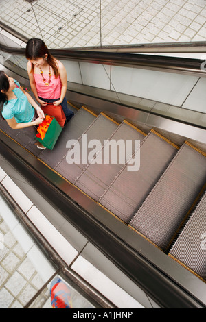 High angle view of two young women standing on an escalator with shopping bags Stock Photo