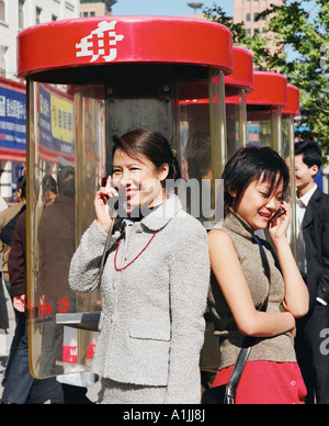 Young woman talking on a pay phone with another young woman talking on a mobile phone Stock Photo