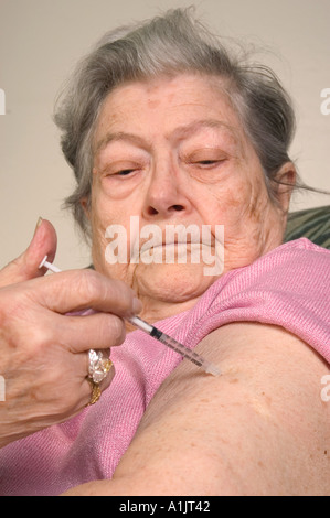 Senior caucasion woman in pink blouse injects insulin into arm with syringe diabetic diabetes Stock Photo