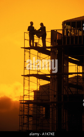 silhouette of workers on scaffolding discussing plans at construction site Stock Photo