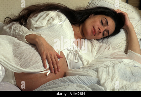 Anglo-Asian Woman in late pregnancy lying down on bed to rest Stock Photo