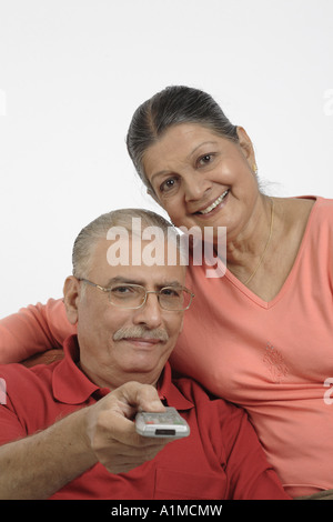 Happy Indian senior citizen couple pressing remote on white background Stock Photo