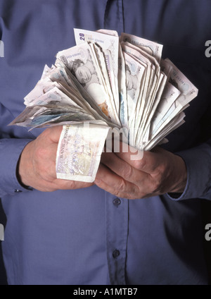 Close up man hoarding & hand gripping holding on stacks of assorted cash in pound sterling money bank notes posed by model studio photo England UK Stock Photo