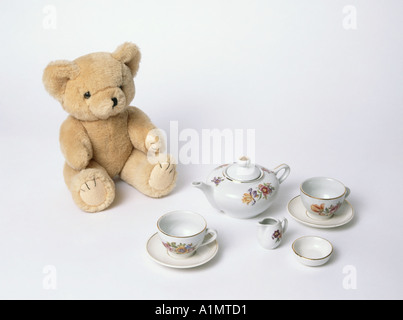 Childs Teddy Bear posed on white background sitting down about to enjoy a nice cup of tea from miniature china toy tea pot set Essex England UK Stock Photo