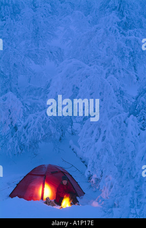 Woman sitting next to campfire and tent in snowy wilderness, Sweden. Stock Photo