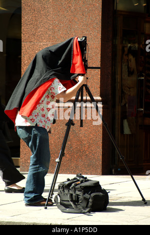 London Piccadilly photographer working with large format camera on tripod with head under a large black and red hood Stock Photo