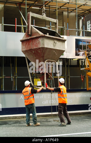 London City of Westminster building site with banksman labourer standing in public highway supervising lowering of crane skip Stock Photo