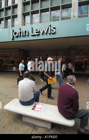 Street scene London West End Oxford Street shoppers outside John Lewis department store front with men sitting on stone seat England UK Stock Photo