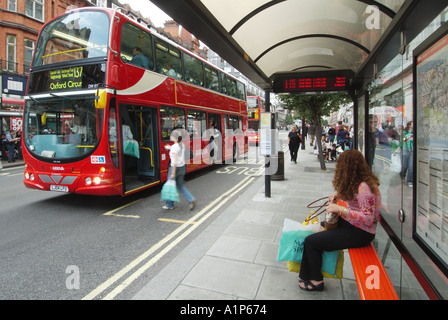 Oxford Street 137 London red double decker bus at public transport bus stop in shopping street shelter seat & passenger boarding West End  England UK Stock Photo