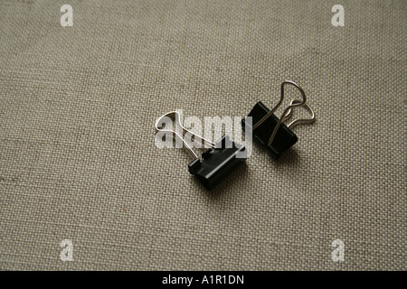 Two black binder clips on a textured fabric surface, useful for organizing and securing papers in offices and schools. Stock Photo