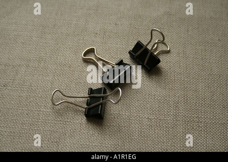 Three black binder clips on a textured fabric surface, perfect for organizing and securing papers in offices and schools. Stock Photo