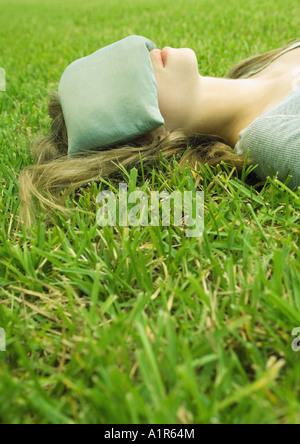 Young woman lying on grass with eye pillow covering eyes Stock Photo