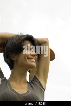 Woman outdoors with arms behind head, holding shoes in hand Stock Photo
