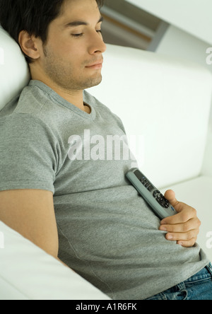 Man sitting on sofa, holding remote control against chest Stock Photo