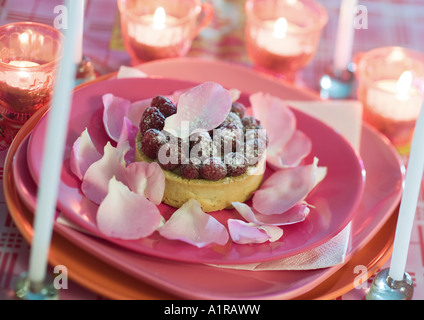 Raspberry tartlet on plate decorated with rose petals, surrounded with candles Stock Photo