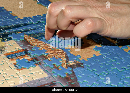 A woman s hand chooses a piece for a mostly blue sky section of a complex jigsaw puzzle of a villa Stock Photo
