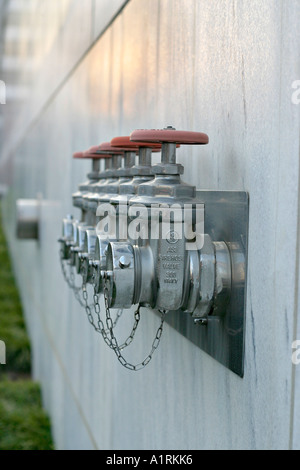 Standpipe Connections: A row of chromed fire hose connectors topped with red valve handles on the side of a marble building Stock Photo