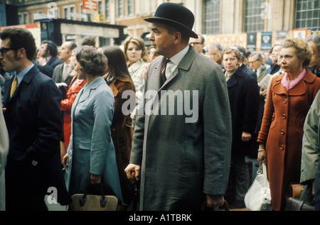 London transport train commuters 1970s UK. Waterloo main line railway station 1972 City gent in bowler hat rolled umbrella crowds wait for late train. Stock Photo