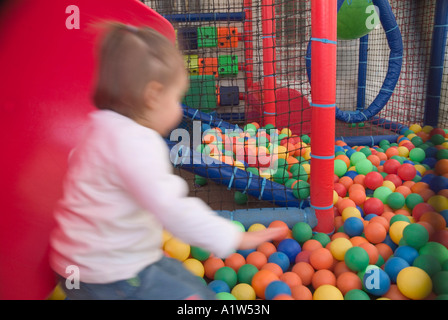 2 year old baby girl sliding down red slide in ball pit Stock Photo