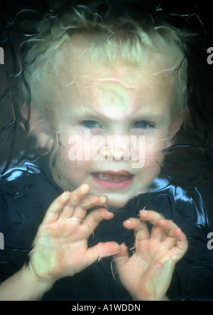 Little Boy Looking Through Patterned Glass Window. Stock Photo