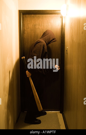 A hooded figure with a baseball bat stands at a doorway Stock Photo