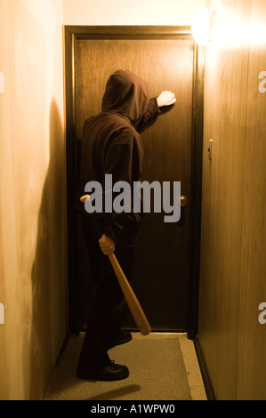 A hooded figure with a baseball bat stands at a doorway Stock Photo