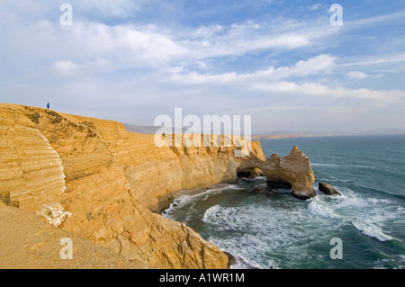 A tourist is dwarfed by an area of the coast and rock formation known as 'The Cathedral' in the Paracas National Reserve. Stock Photo