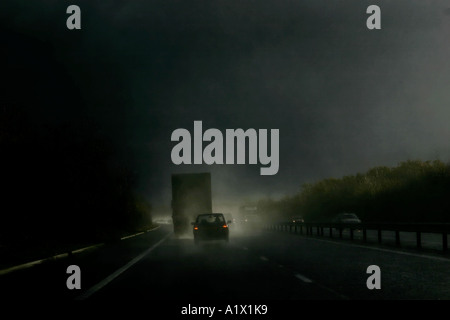 heavy spray caught by sunshine during heavy rain coming from lorry on M4 motorway england with car following showing brake light Stock Photo