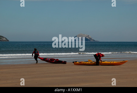 Yellow and red canoes being prepared by a man and woman to sail in the North Sea off Scottish be with Bass Rock in background Stock Photo