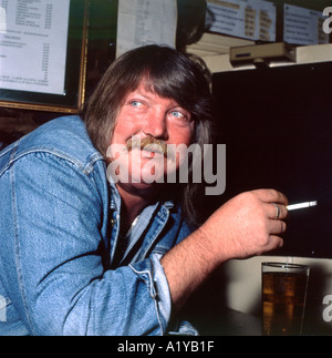A man with blue eyes and wearing a denim jacket smiling, smoking and drinking in Brown's Hotel, Laugharne, Wales,UK  KATHY DEWITT Stock Photo