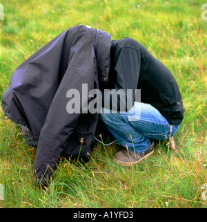 Man with head under his black coat jacket crouching in a field in Wales UK  KATHY DEWITT Stock Photo