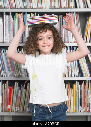 Girl balancing stack of books on head in library, portrait Stock Photo