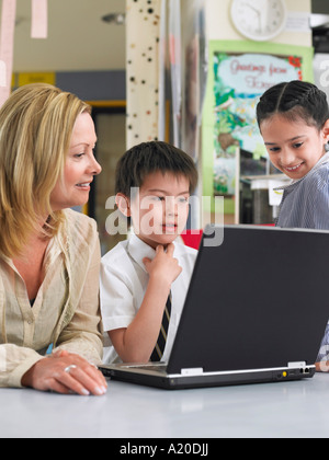 Teacher sitting with students using laptop in classroom Stock Photo