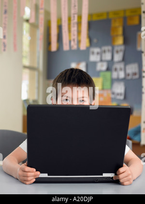 Elementary schoolboy sitting behind opened laptop in classroom Stock Photo
