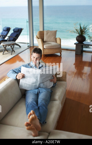 Man lying on sofa, reading newspaper, elevated view. Stock Photo