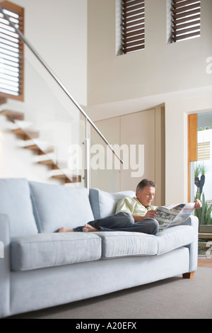 Mid-adult Man reclining on sofa, Reading Newspaper Stock Photo