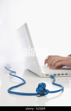 Woman using lap top with knotted cable in studio, close up on knot Stock Photo