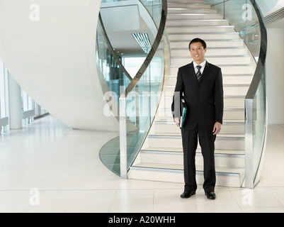Confident Businessman, holding folder, standing in front of stairs Stock Photo