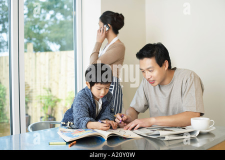Father and Son coloring in Coloring Book on table, mother talking on mobile Stock Photo