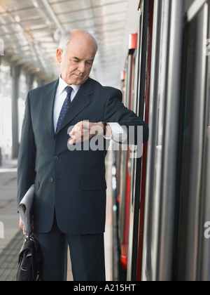 Mature Businessman checking time, standing outside train in station Stock Photo